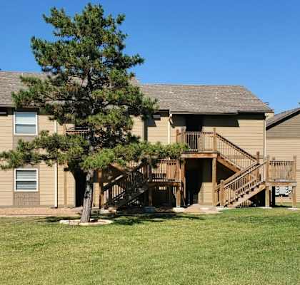 A side view of the Willow Creek Apartment building with brown walls, surrounded by green grass and a tree in front.