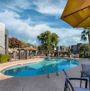 A pool area with a table and chairs and a yellow umbrella. at Tela Verde, Glendale, AZ, 85306