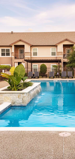 A pool surrounded by a fence and chairs in front of a building.