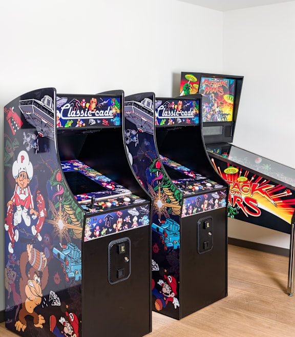 Two arcade style game machines with a table and chairs in between.