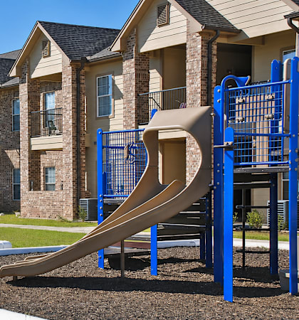 A playground with a slide and a building in the background.