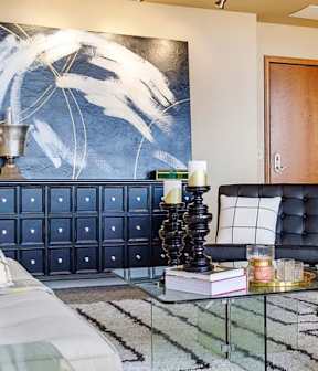 A modern living room with a black couch and a large painting on the wall.