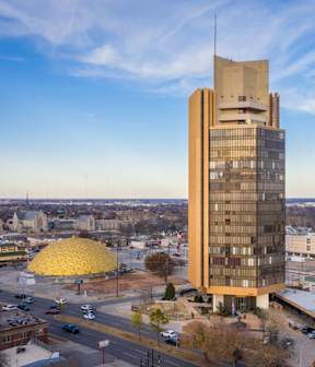 A tall building with a golden dome in the foreground and a cityscape in the background.