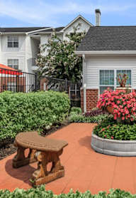 A patio with a bench and a planter with red flowers.