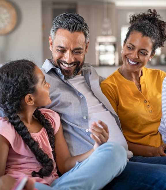 A family of four is sitting together on a couch.