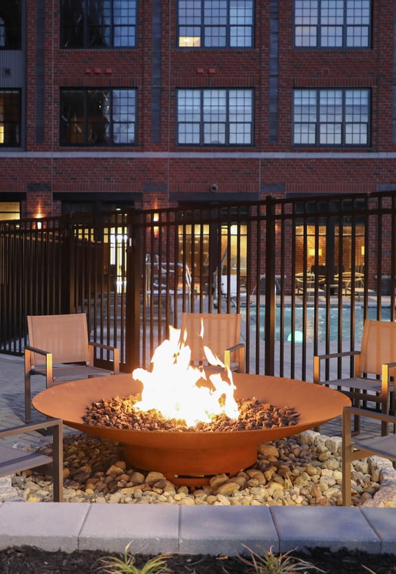 a fire pit with chairs and a building in the background at The Met at Metro Centre Apartments, Owings Mills Maryland