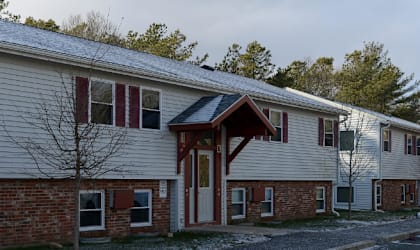 A building with a red brick wall and a white siding with a car parked in front.