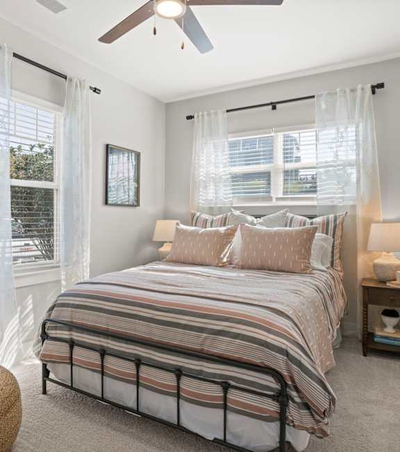 A bedroom with a bed, a ceiling fan, and a window with curtains.
