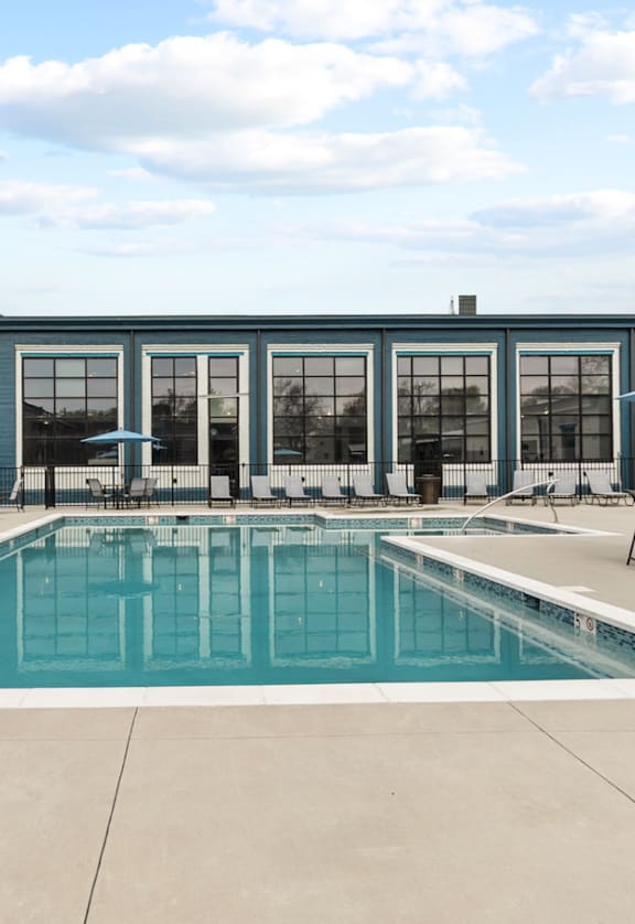 a swimming pool with lounge chairs and umbrellas in front of a brick building