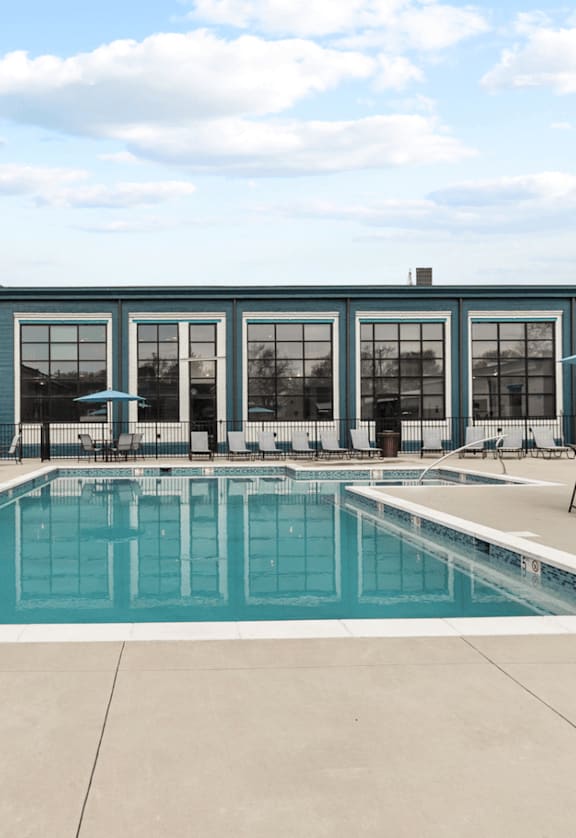 a swimming pool with lounge chairs and umbrellas in front of a brick building