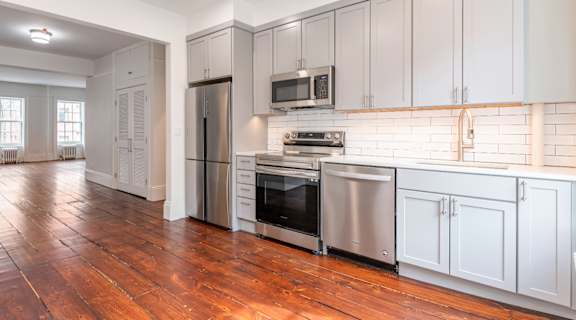 a kitchen and living room with white cabinets and wood floors
