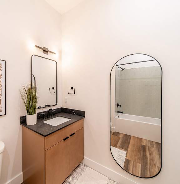 A bathroom with a toilet, sink, mirror and a picture on the wall.