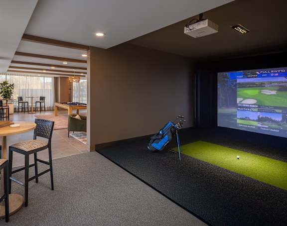 A room with a golf simulator and a dining table.