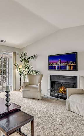 A living room with a fireplace, two chairs, and a potted plant.