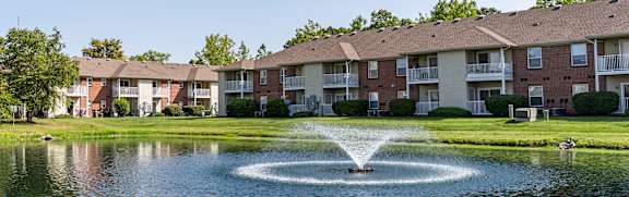A fountain in the middle of a pond in front of apartment buildings.