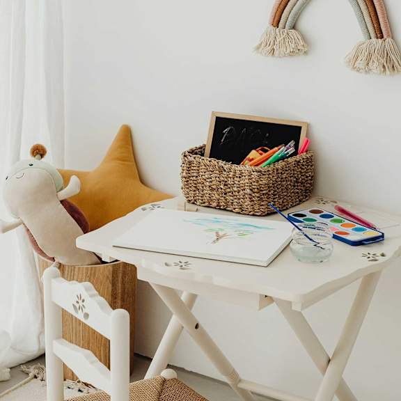 A white desk with a yellow star-shaped pillow and a white chair with a wooden design.