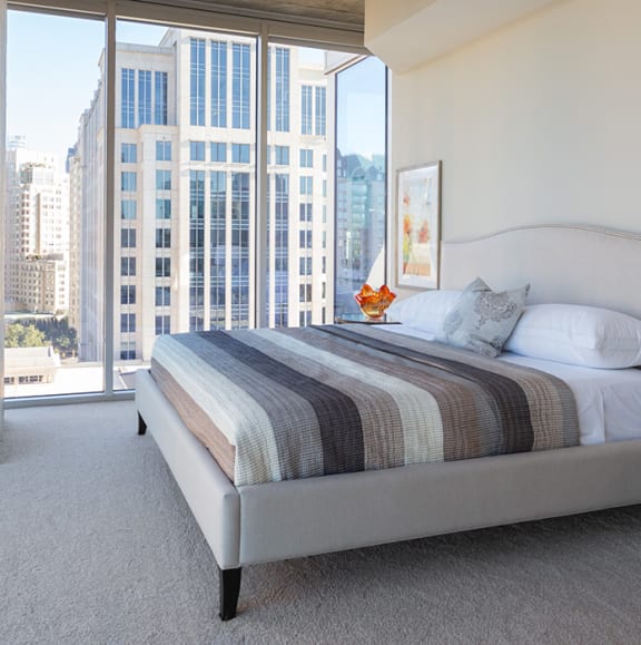 a bedroom with floor to ceiling windows overlooking downtown