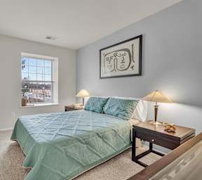 A bedroom with a bed, nightstand, and a painting on the wall.