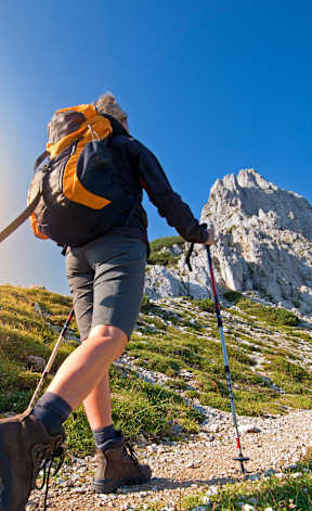 A hiker with a backpack and trekking poles is walking on a rocky trail in the mountains.