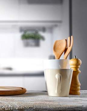 A kitchen counter with a cup, a plate, a wooden spoon, and a pepper grinder.