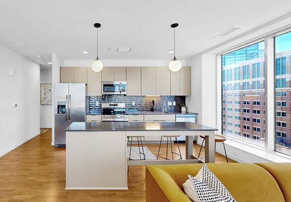 A modern kitchen with a yellow couch and a view of the city.