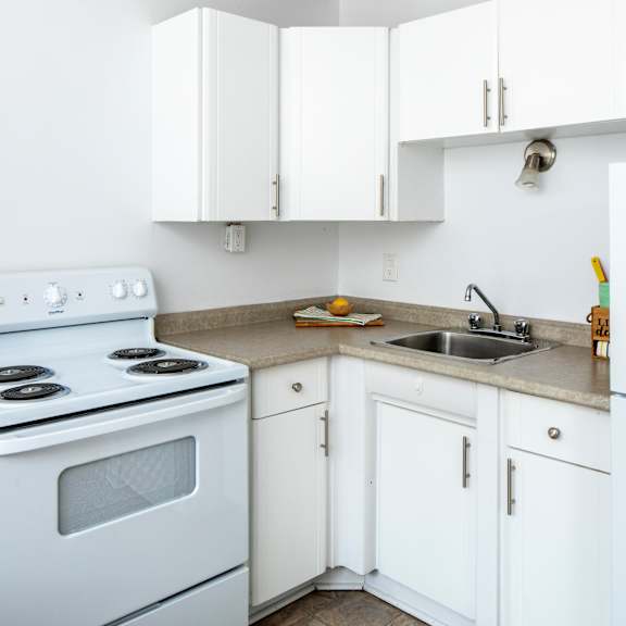 A white kitchen with a stove, sink, and cabinets.