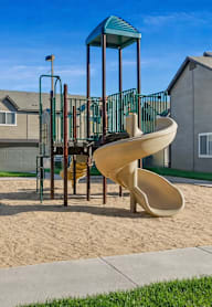 A playground with a slide and a swing set in the foreground and apartment buildings in the background.