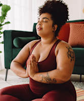 A woman in a red outfit is meditating on a yoga mat.