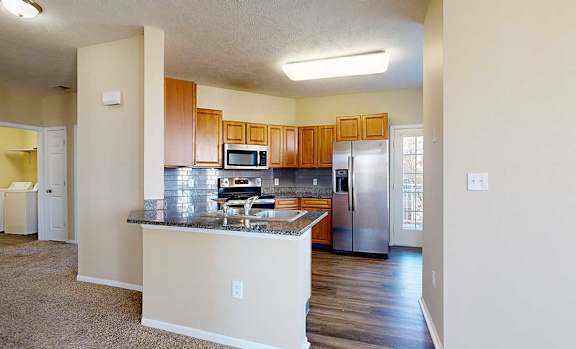 a kitchen featuring wooden cabinets, granite countertops, a peninsula, a tile backsplash, hardwood floors, and stainless steel appliances