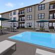 A pool with loungers and umbrellas is surrounded by a building.