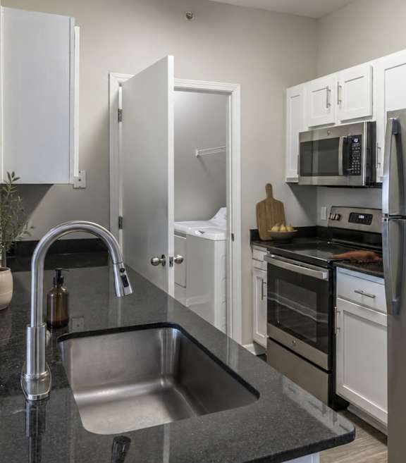 A kitchen with a black counter top and stainless steel appliances.