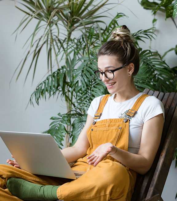 A woman in a yellow jumpsuit is sitting on a chair with a laptop in front of her.