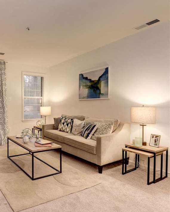 A living room with a couch, chair, ottoman, and a table with a lamp on it.