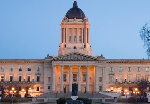 A large, grand building with a dome and a flag on top is illuminated and stands alone.