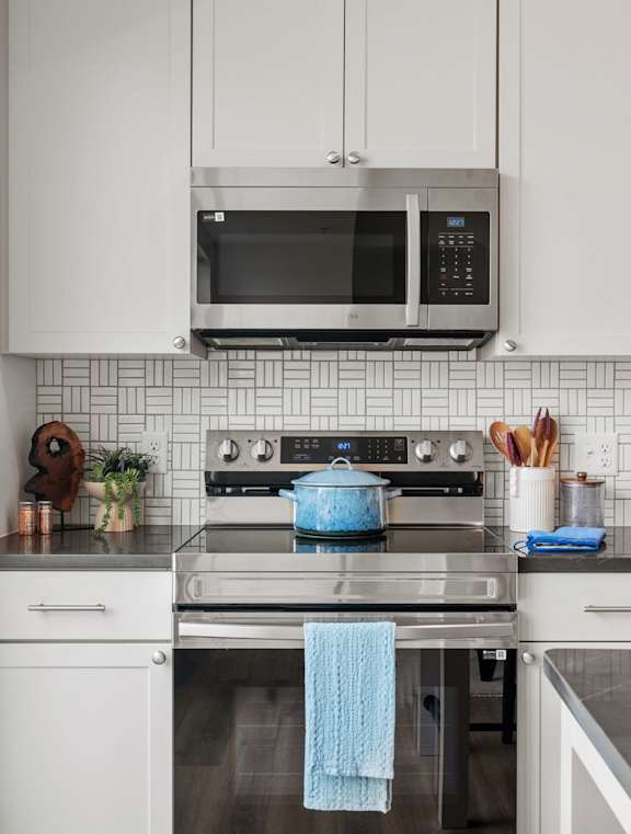A modern kitchen with white cabinets and a blue towel hanging on the oven.