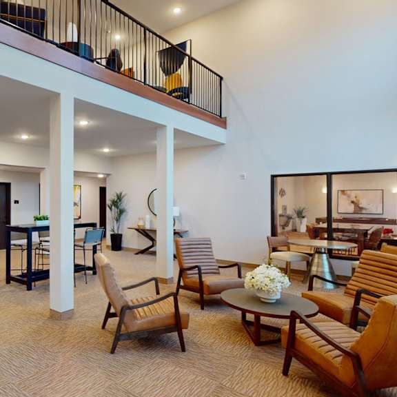 The resident lounge with tables, chairs, comfortable leather chairs with a coffee table with flowers on it at the Club at Heritage Apartment Homes. 