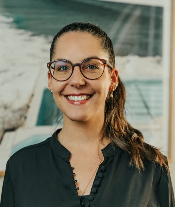 a woman wearing glasses standing in front of a painting
