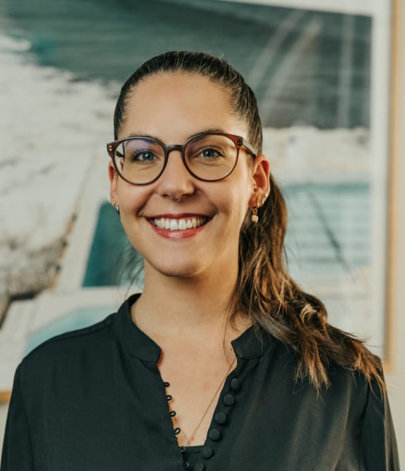 a woman wearing glasses standing in front of a painting