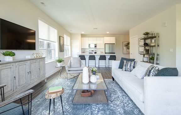 A modern living room with a white couch, a wooden coffee table, and a flat-screen TV mounted on the wall.