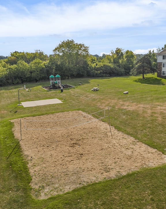A large grassy field with a dirt mound in the center and a green structure in the background.