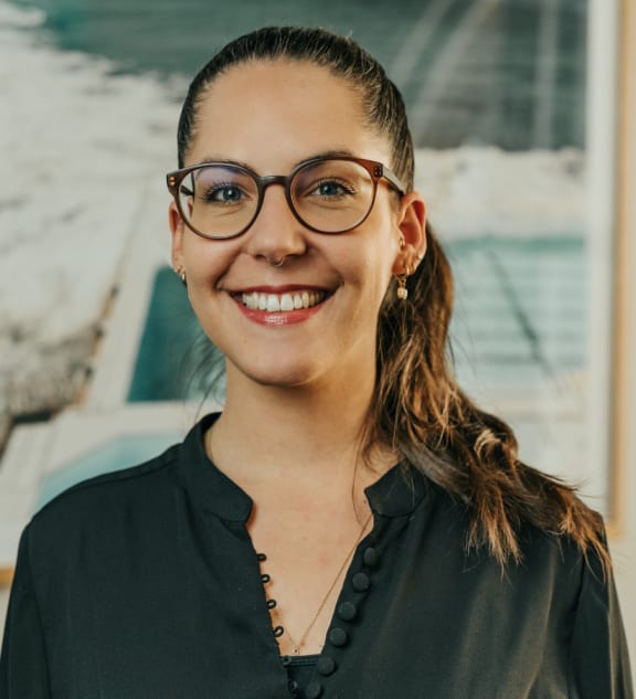 a woman wearing glasses standing in front of a painting
