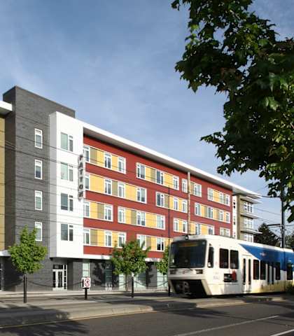 A modern multi-story building with a white and red facade stands next to a street with a tram.