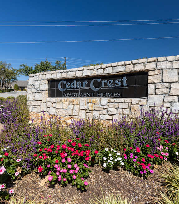 The Cedar Crest Apartments sign displayed in front of a stone wall, surrounded by flowers and landscaping.