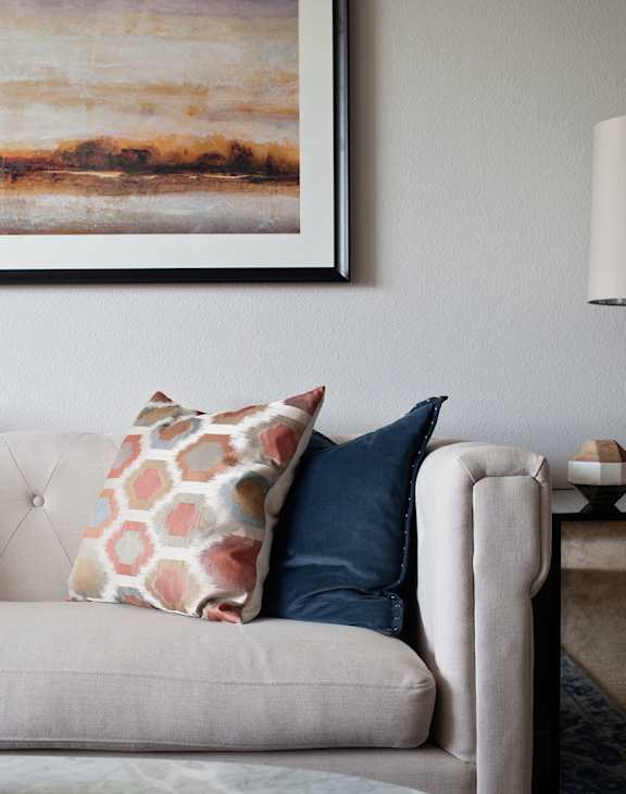 A living room with a grey couch, a lamp, and a painting on the wall.