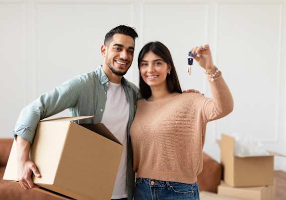 A man and woman are standing in a room with boxes, holding a key and a box at The Lodge at Lakeline Village, Cedar Park, TX, 78613