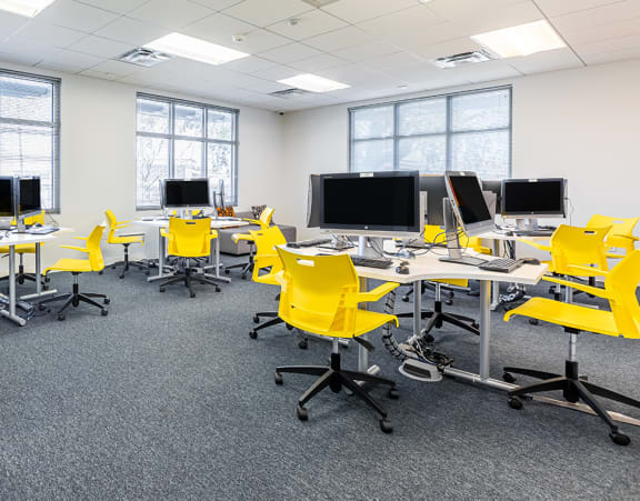 an empty classroom with yellow chairs and desks and computers