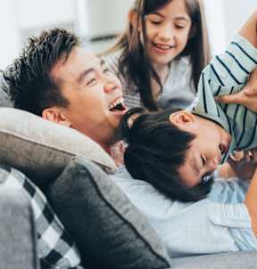 a father and daughter sitting on a couch playing with a dog