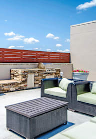 A stone fireplace is the centerpiece of a patio with a couch, chairs, and a table. at Vivant Woodholme, Pikesville