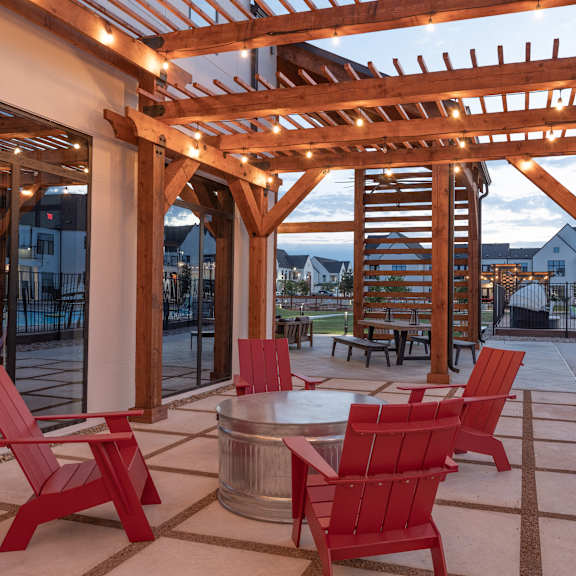 A wooden pergola with red chairs and a table is set up outside.