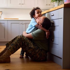 a woman in camouflage pants and a green shirt holds a young girl in a kitchen
